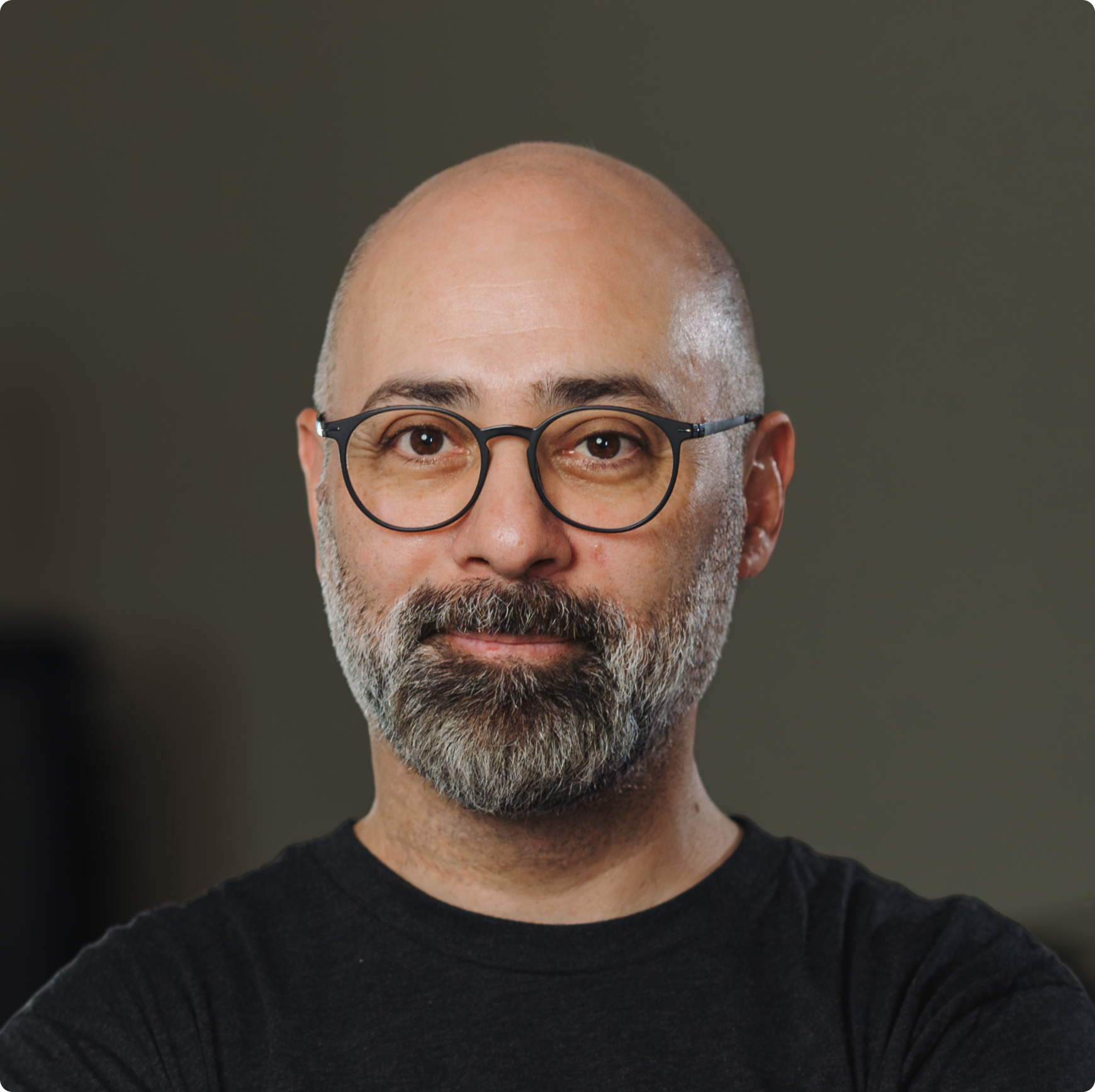 Smiling middle-aged bald man with a salt-and-pepper beard and round glasses wearing a black shirt.